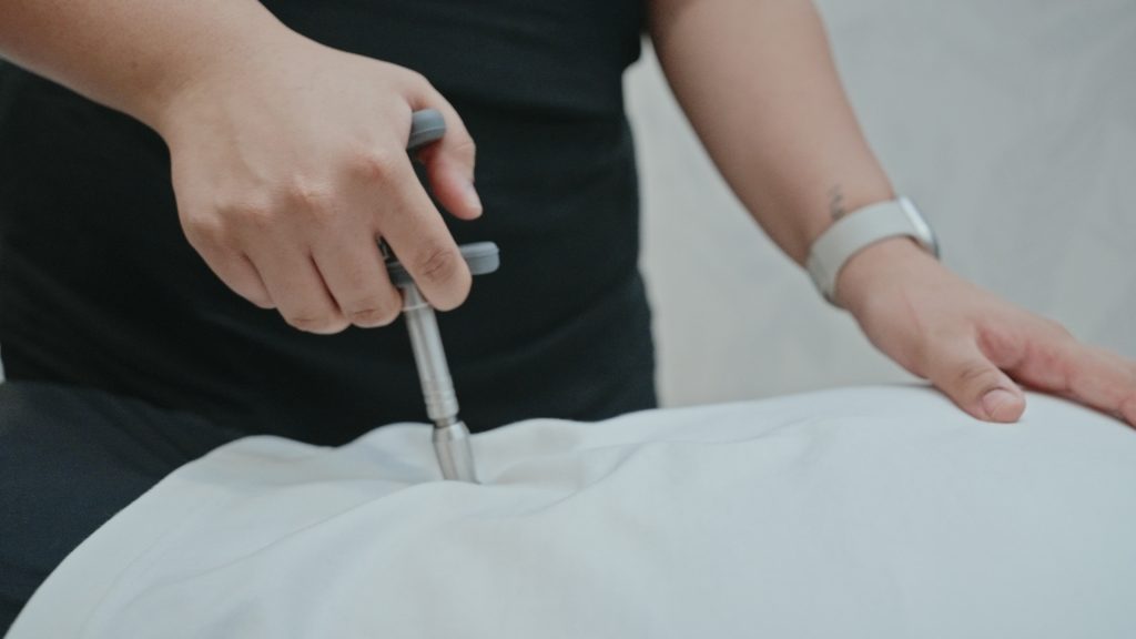 Chiropractor using a handheld adjustment tool on a patient’s lower back during treatment