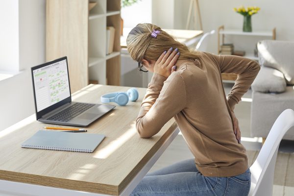 Woman sitting at a desk holding her lower back and neck, showing posture-related back pain treated at Radiant Chiropractic in Canterbury, Eastern Melbourne.