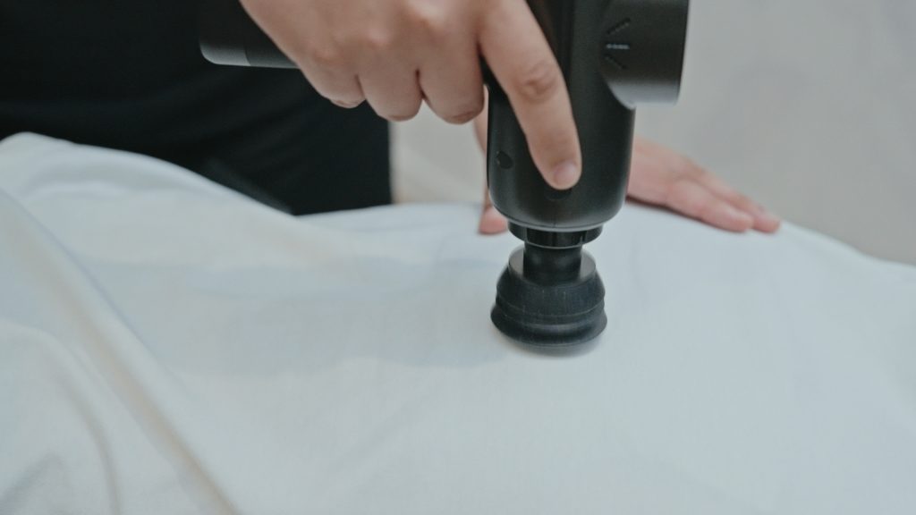 Chiropractor using a handheld adjustment instrument on a patient’s lower back during treatment