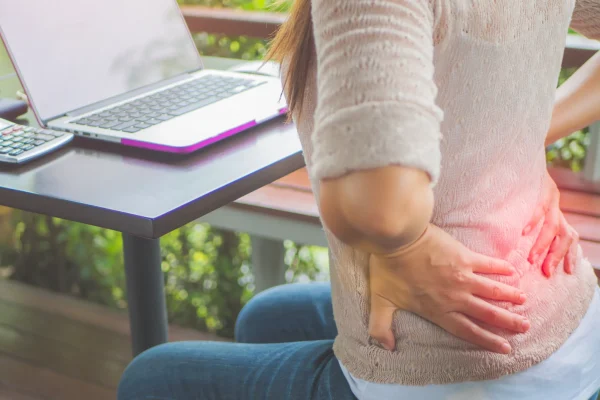 Woman sitting at a desk holding her lower back in pain, illustrating work-related lower back pain treated at Radiant Chiropractic in Canterbury, Eastern Melbourne.