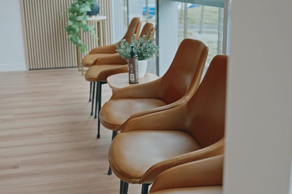 Row of comfortable tan leather chairs in a modern chiropractic clinic waiting area with wooden flooring and natural light.