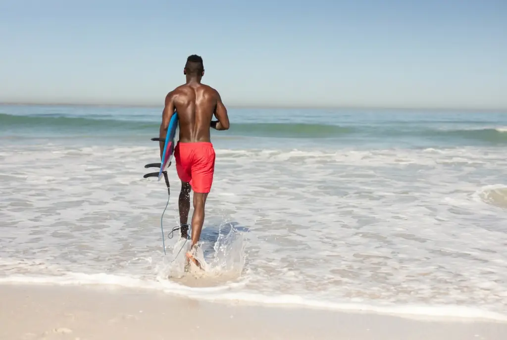 Surfer walking into the ocean carrying a surfboard, representing active movement